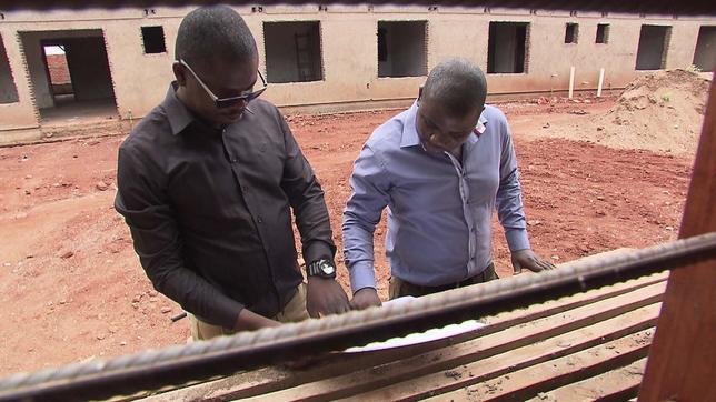 Zwei afrikanische Architekten beraten vor einem Rohbau über einem Bauplan.