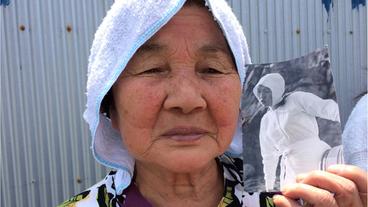 Eine alte Ama-Taucherin hält ein Bild von sich als junge Frau in der traditionellen Kleidung in der Hand.