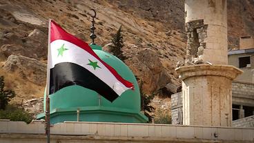 Die syrische Flagge weht über zerstörten Häusern in Damaskus.