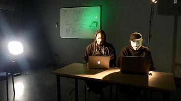 Zwei maskierte Männer sitzen an Laptops.
