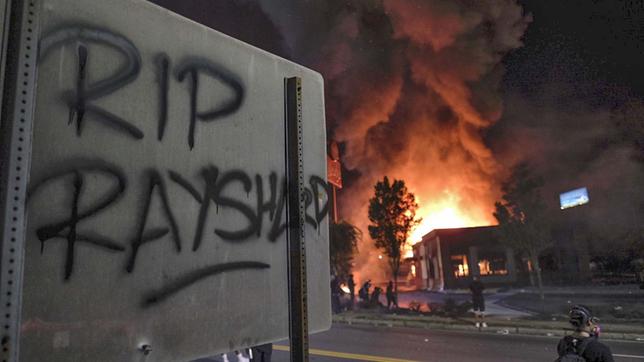 "RIP Rayshard" steht auf einem Schild, während im Hintergrund ein Wendy's-Restaurant brennt