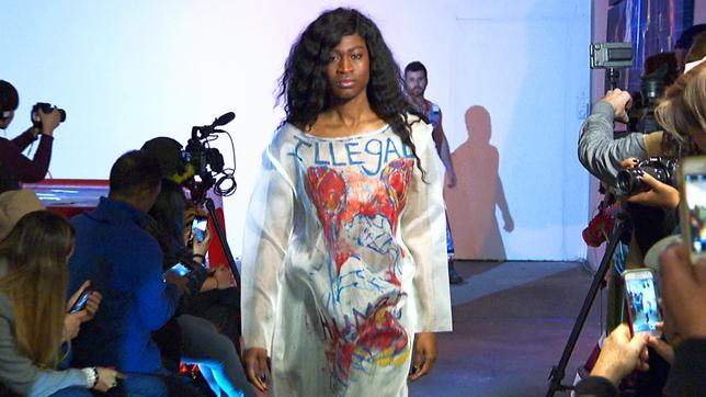 Ein Model läuft in einem Kleid, auf dem "Illegal" geschrieben steht.