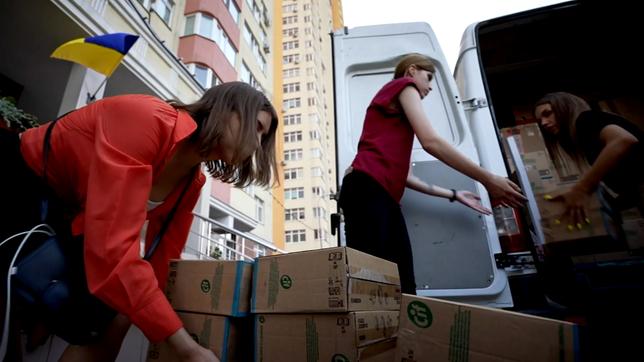 Frauen packen Kartons aus einem Transporter aus.