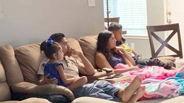 Vierköpfige Familie schaut Fernsehen und sitzt auf einem Sofa.