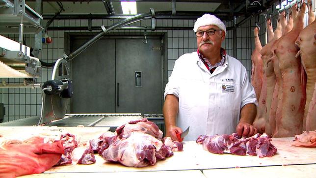 Fleischer steht am Tisch und schneidet Fleisch