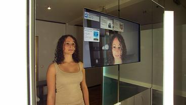 Junge Frau steht vor einem Monitor im Spiegel