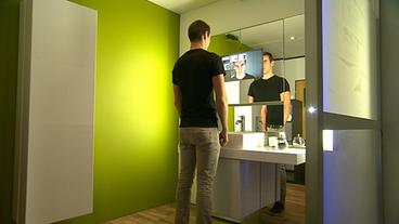 Junger Mann steht vor einem im Spiegel eingelassenen Monitor