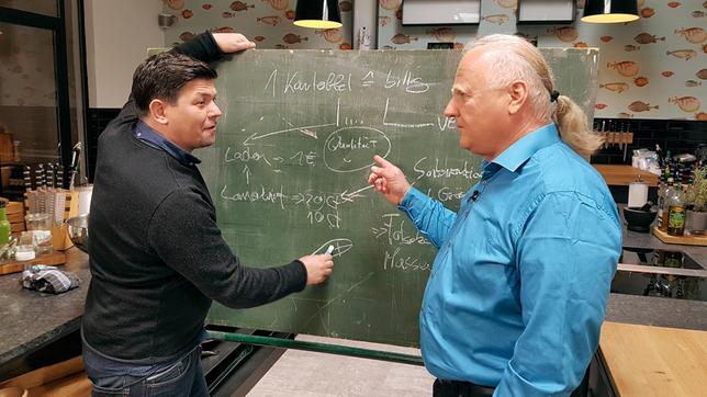 Bild: NDR/Axel Thiede Bioland-Pressesprecher Gerald Wehde erklärt Tim Mälzer, dass Lebensmittel viel teurer für uns sind, als wir an der Supermarktkasse zahlen.