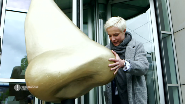 Bild: MDR Reporterin Seraphina Kalze mit einer Skulptur „Goldene Nase“ vor dem Gebäude des Verbands der Kosmetikindustrie.