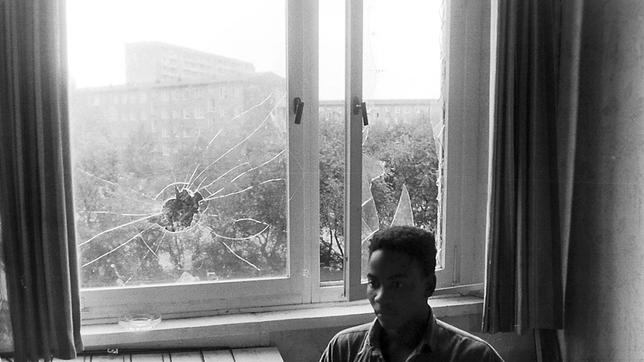 Ein mosambikanischer Vertragsarbeiter in seinem Wohnheimzimmer, im Hintergrund die eingeworfenen Fensterscheiben.