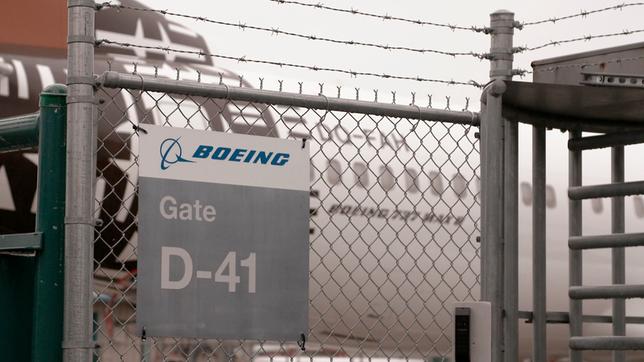 Ein Zaun mit der Beschriftung "Boeing Gate D-41". Im Hintergrund ist ein Flugzeug zu sehen.