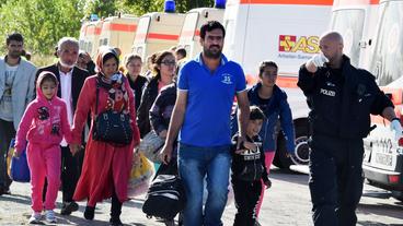 Ein Polizist begleitet am 8. September am Bahnhof in Schönefeld (Brandenburg) Flüchtlinge zum Bus, der sie weitertransportieren soll.  
