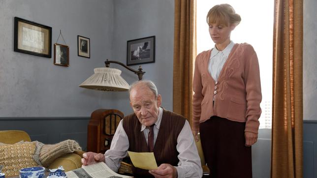 Bild: NDR/DOKfilm/Carsten Schick Im Exil in Schleswig 1947: In der Wohnung seiner ältesten Tochter Margarethe (Christina Große) betrachtet der Helgoländer Fotograf Franz Schensky (Michael Mendl) Bilder seiner Vergangenheit, darunter sein Hochzeitsfoto. Kurz zuvor wurde in einer Meldung der Termin für die von den Briten geplante Sprengung auf Helgoland bekanntgegeben, der „Big Bang“.