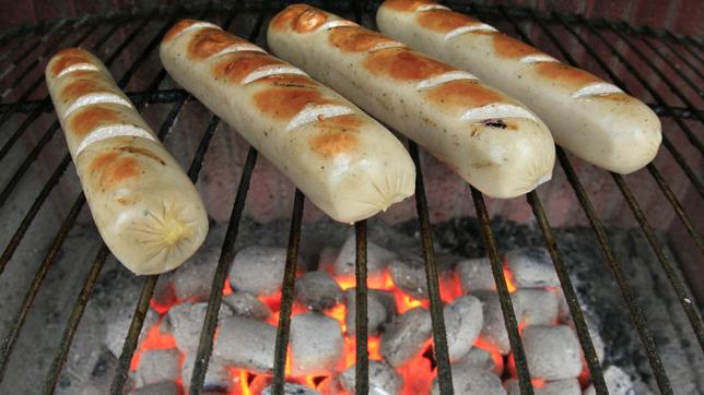 Bratwürstchen liegen auf einem Grill mit glühender Kohle.