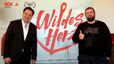 Bild: dpa Bei der deutschlandweiten Kinopremiere des Dokumentarfilms "Wildes Herz" über die Punkband "Feine Sahne Fischfilet" stehen Regisseur Charly Hübner (l-r) und der Frontmann der Band Jan "Monchi" Gorkow vor einem Aufsteller