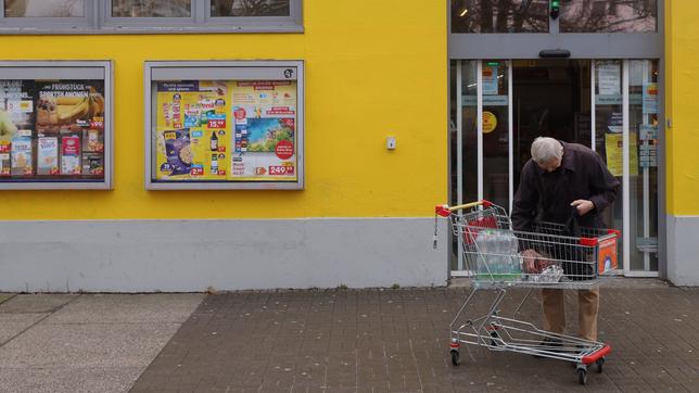 Älterer Mann mit Einkaufswagen vor einem Supermarkt
