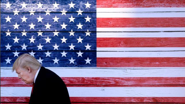 Donald Trump steht mit gesenktem Kopf vor einer US-Flagge