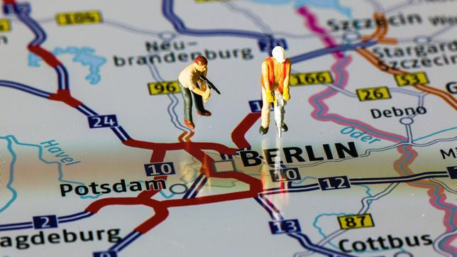Zwei Modellfiguren, die Bauarbeiter darstellen, stehen auf einer Landkarte, die das Autobahnnetz um Berlin zeigt. 