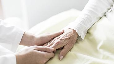 Die Hand einer Pflegerin hält die Hand einer alten Frau.
