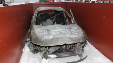 Ein ausgebranntes Auto steht in einem Container in den Resten von Löschschaum.