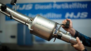 Bild: picture alliance/Ina Fassbender Ein Mechaniker hält einen Katalysator hoch.