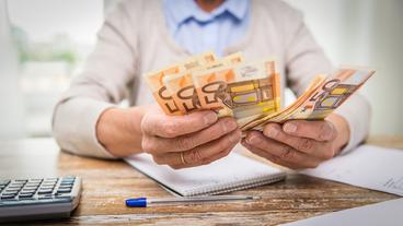 Die Hände eines älteren Mannes halten mehrere 50 Euro Scheine aufgefächert über einen Tisch.