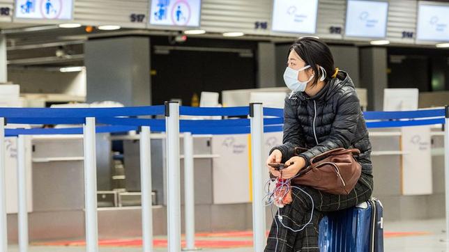 Bild: picture alliance/dpa /Andreas Arnold Eine asiatische Frau sitzt auf einem Koffer vor dem Check-in Schalter