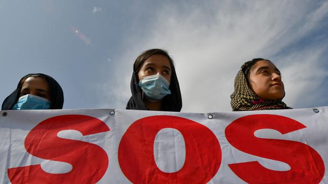Drei junge Frauen mit Kopftuch halten ein Schild mit der Aufschrift "SOS".