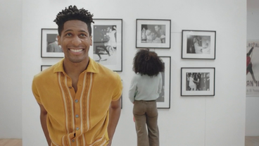 Bild: Screenshot Jon Batiste lächelt. Hinter ihm steht eine Frau.