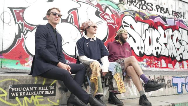 Drei Personen sitzen vor einer Graffitiwand