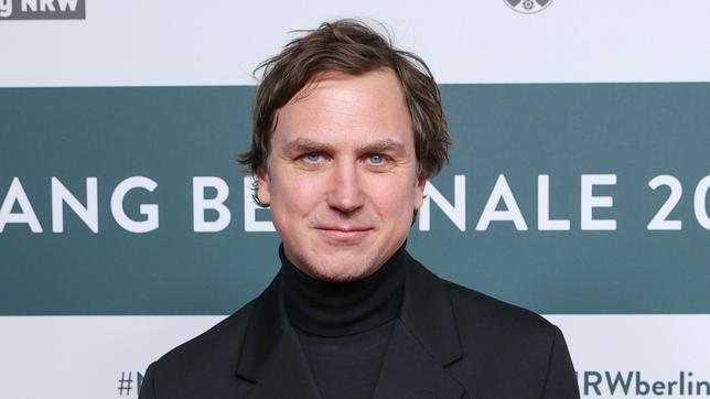 Lars Eidinger schaut in die Kamera und lächelt.
