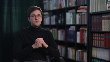 Ein junger, Weißer Mann mit dunklen Haaren und Brille sitzt vor einem Bücherregal. Es ist der Autor und Journalist Ole Nymoen.