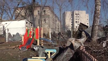 Ein Spielplatz, auf dem Müll und Schrott liegen, im Hintergrund ausgebombte Häuser. Es ist eine Szene in der Ukraine.