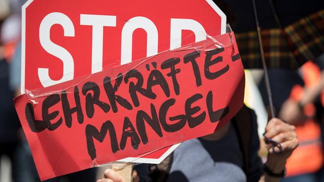 Ein Schild wird hochgehalten auf dem steht: "Stop Lehrkräftemangel".