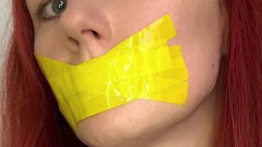 Eine rothaarige Frau trägt über dem Mund zwei gelbe Klebestreifen.