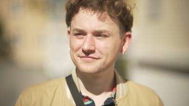 Bild: NDR Ein Mann mit kurzen lockigen Haaren und silbernen Kreolen in den Ohren lächelt in die Sonne: Jonas Löschau.