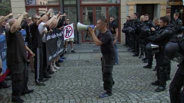 Bild: NDR Menschen heben die geballten Fäuste und werden von einem Mann mit Megafon angefeuert. Vis-a-vis steht ein Polizeitrupp.