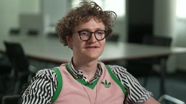 Bild: NDR Eine Person mit kurzen lockigen Haaren, Brille und einem rosa Pollunder über einem gestreiften Hemd: Lorenz Blumenthaler.