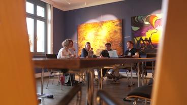 Bild: NDR Vier Menschen sitzen an einem Tisch an Laptops und unterhalten sich.