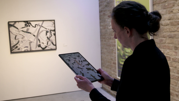 Bild: Screenshot Anika Meier schaut auf ein Tablet in ihrer Hand.