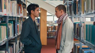 Bild: © Les Films Grand Huit Zwei Männer stehen sich zwischen den Regalen einer Bibliothek gegenüber.