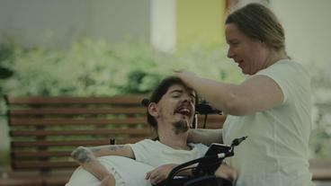 Ein Mann im Rollstuhl wird von einer Pflegerin gekämmt