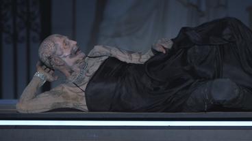 Bild: BR Ein am ganzen Körper tätowierter Mann räkelt sich im schwarzen Abendkleid auf einer Opernbühne