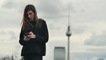 Eine junge Frau auf einem Hausdach, mit Blick auf ihr Handy