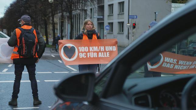 Eine junge Frau mit Transparent in der Hand hindert Autos am Weiterfahren