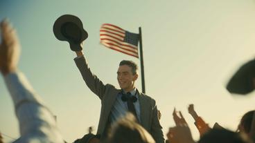 Filmstill eines Mannes, der vor einer US-amerikanischen Flagge steht und winkt