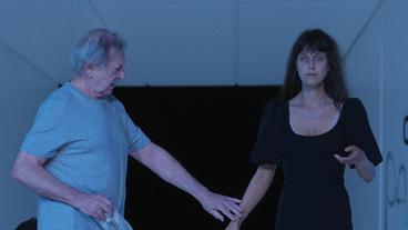 Ein Mann und eien Frau reichen sich auf einer Theaterbühne die Hand