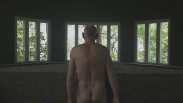Ein nackter Mann steht vor einem Fenster