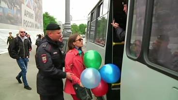 Eine Frau mit bunten Ballons in der Hand wird von einem Polizisten abgeführt