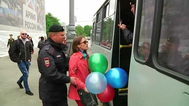 Eine Frau mit bunten Ballons in der Hand wird von einem Polizisten abgeführt